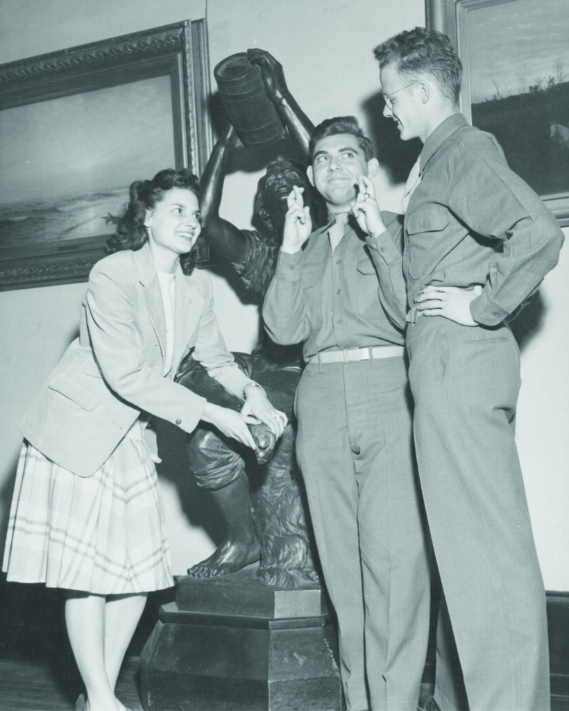 A black and white photo of three Drexel students, two in Army uniforms and one in civilian clothes, leaning against a statue.