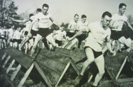A black-and-white photo of a large group of Army cadets navigating an obstacle course.