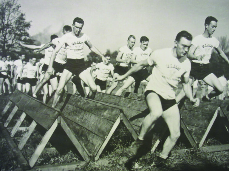 A black-and-white photo of a large group of Army cadets navigating an obstacle course.