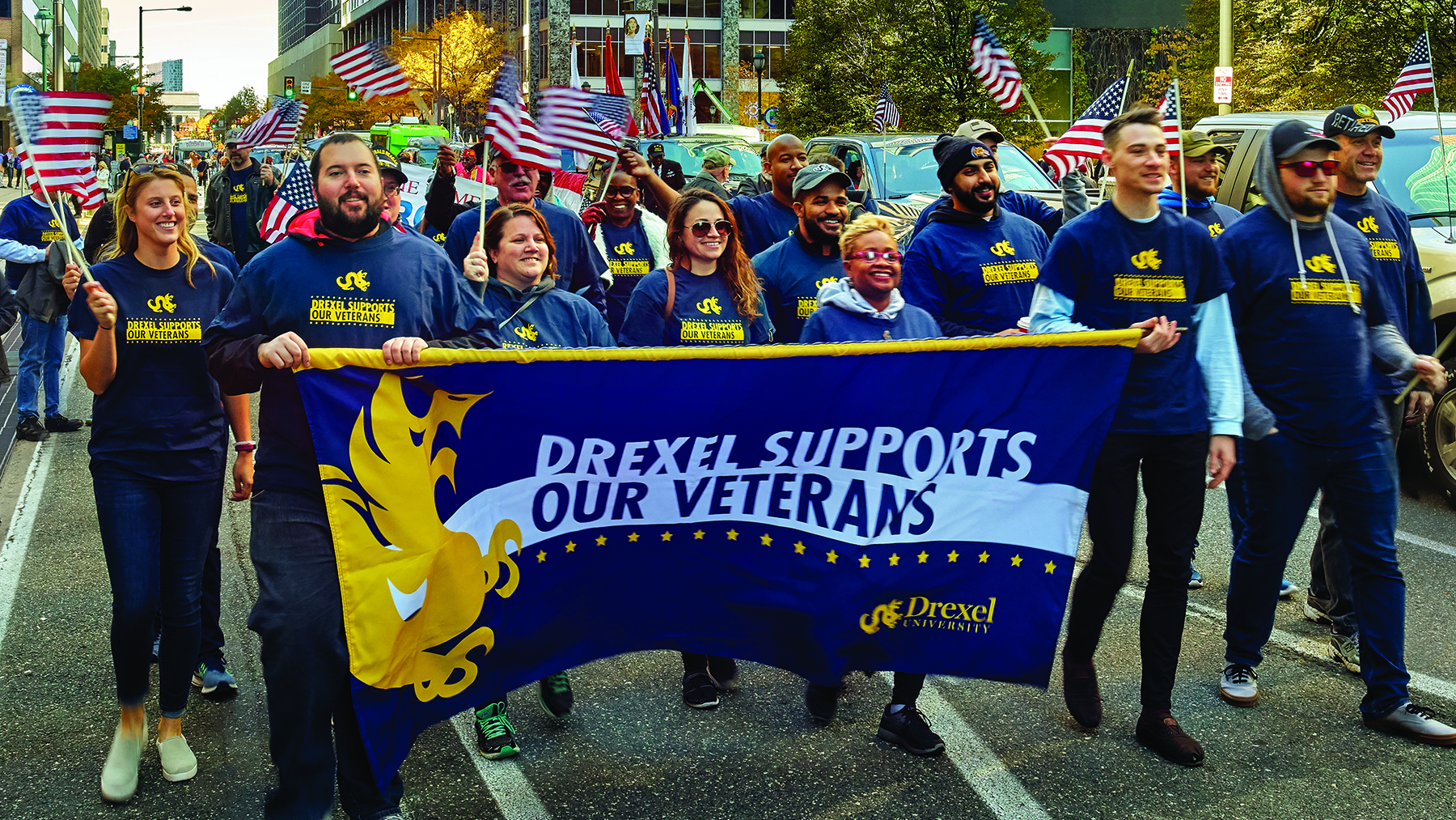 A group of people walk down a Philadelphia street carrying a banner that reads, "Drexel Supports Our Veterans."