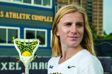 Karson Harris, a white womanwith long blond hair, stands on Daskalakis Athletic Field in her lacrosse uniform.