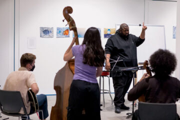 A group of musicians being lead in rehearsal by their conductor